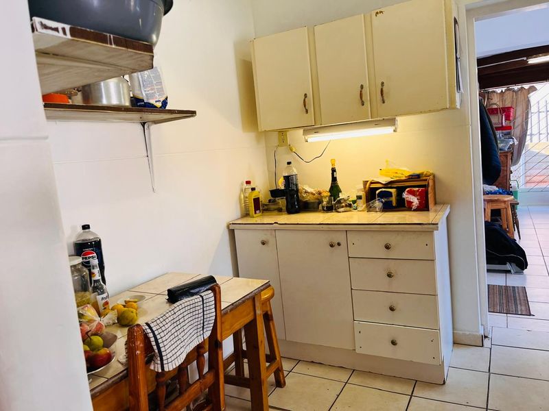 A compact kitchen area featuring tiled flooring, laminate cabinetry, and a tiled countertop with under-cabinet lighting, offering a functional but dated preparation space.