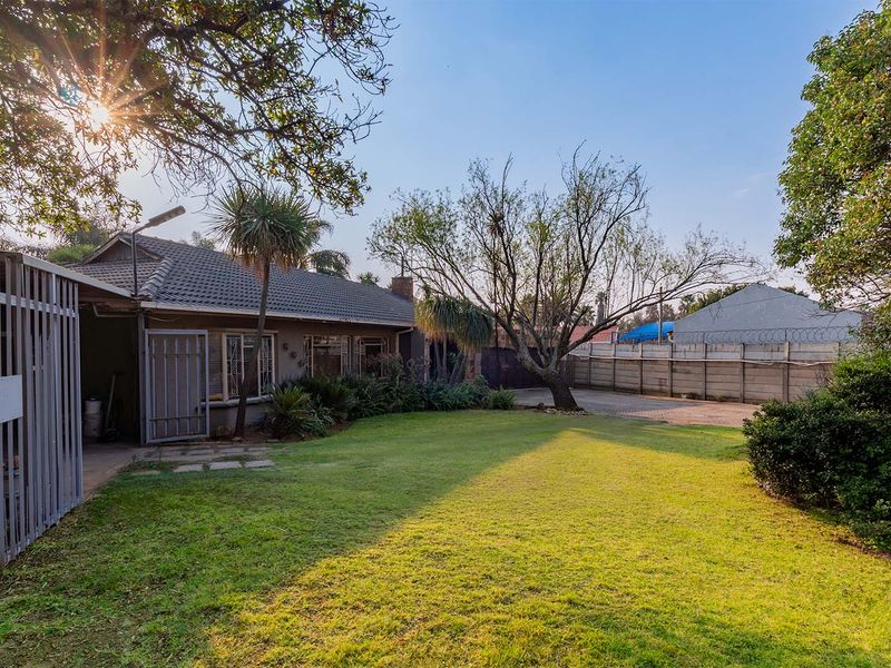A spacious rear garden featuring a well-maintained lawn, paved driveway area, and secure perimeter walling, providing a private outdoor space.