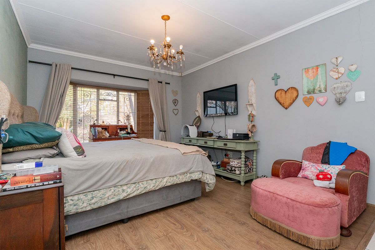 A spacious bedroom featuring laminate flooring, crown molding, a classic chandelier, and a large bay window with security bars.