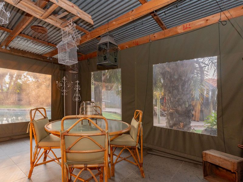 Covered outdoor patio area featuring a corrugated metal roof, timber rafters, and roll-up canvas blinds, overlooking the garden and pool area.