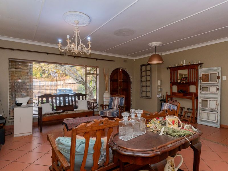 Spacious living area featuring tiled flooring, an arched wooden door, and classic ceiling roses with a decorative chandelier.