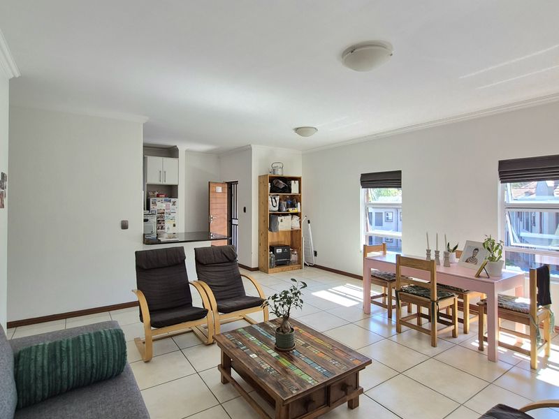 Spacious open-plan living and dining area featuring neutral tiled flooring, ample natural light from large windows, and an integrated kitchen space.