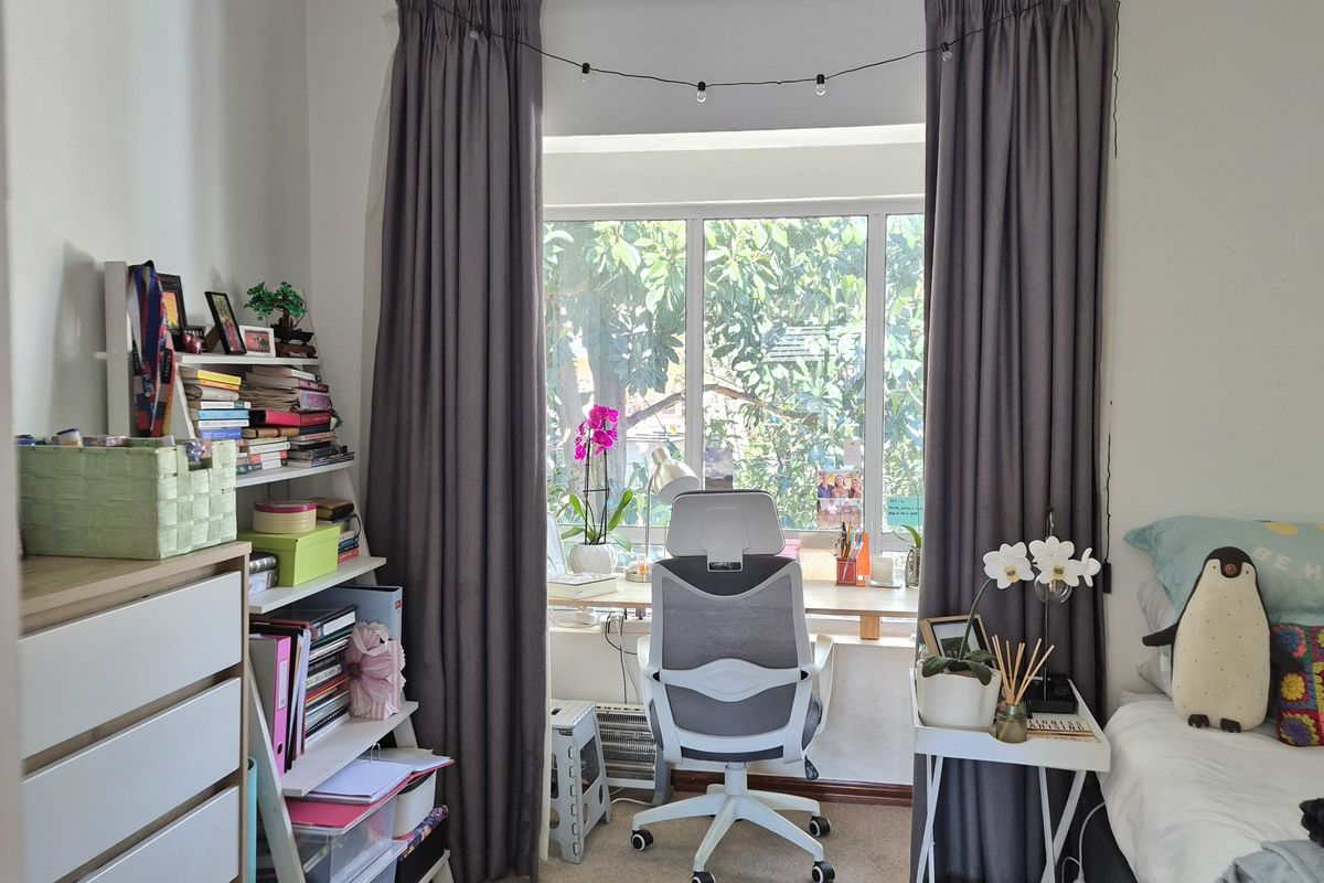 A well-lit bedroom featuring neutral carpet flooring, crown molding, and a large window with curtain tracks, providing a comfortable and functional living space.