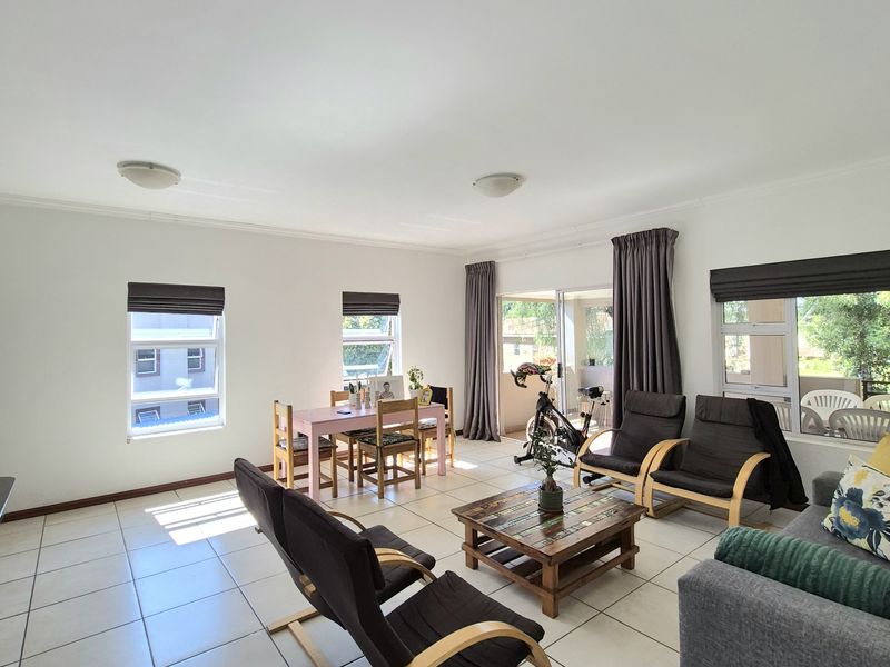Spacious open-plan living and dining area featuring neutral tiled flooring, large windows for natural light, and direct access to an outdoor patio.