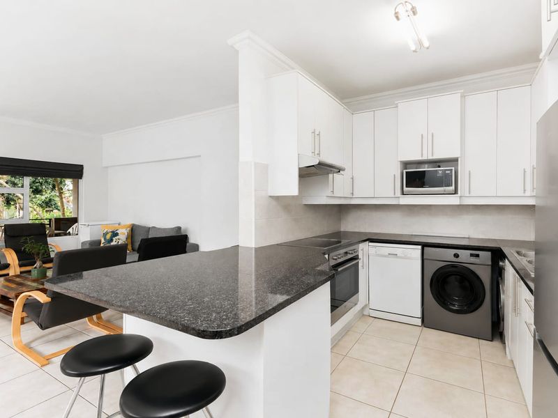 Open-plan kitchen featuring granite countertops, built-in appliances, and a breakfast bar, seamlessly flowing into the adjacent living area with tiled flooring throughout.