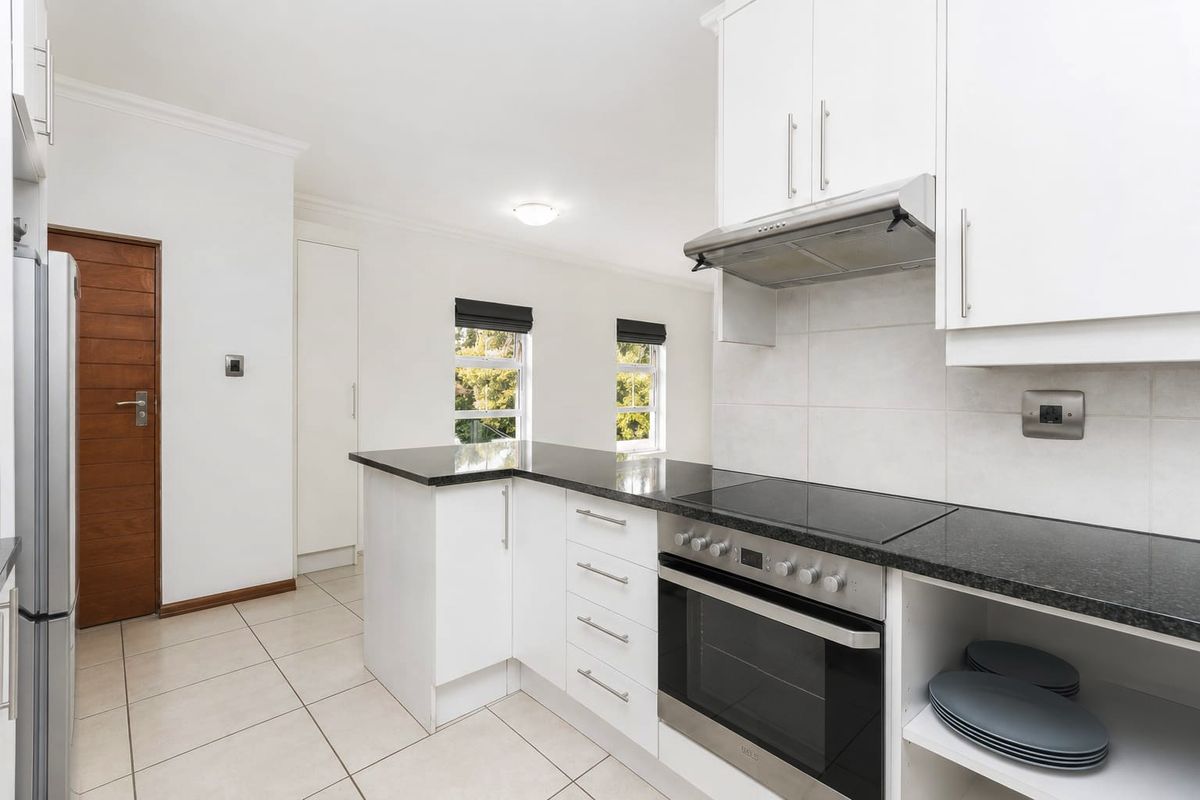 Modern kitchen featuring white cabinetry, granite countertops, built-in oven, electric hob, and extractor fan with tiled flooring.