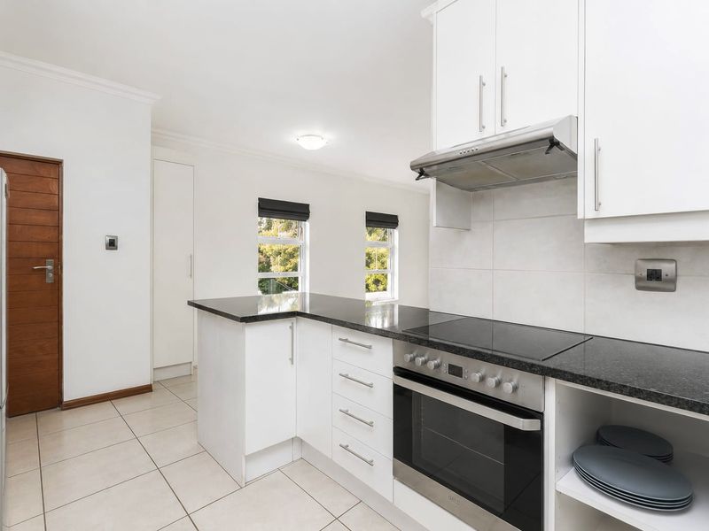 Modern kitchen featuring white cabinetry, granite countertops, built-in oven, electric hob, and extractor fan with tiled flooring.