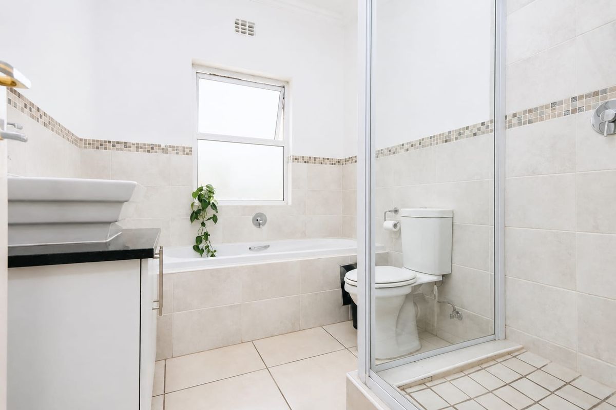 A clean, well-maintained bathroom featuring a built-in vanity, bathtub, separate shower enclosure, and neutral wall and floor tiling.
