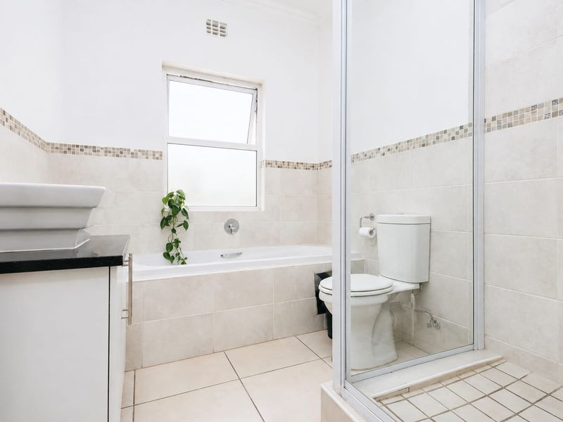 A clean, well-maintained bathroom featuring a built-in vanity, bathtub, separate shower enclosure, and neutral wall and floor tiling.