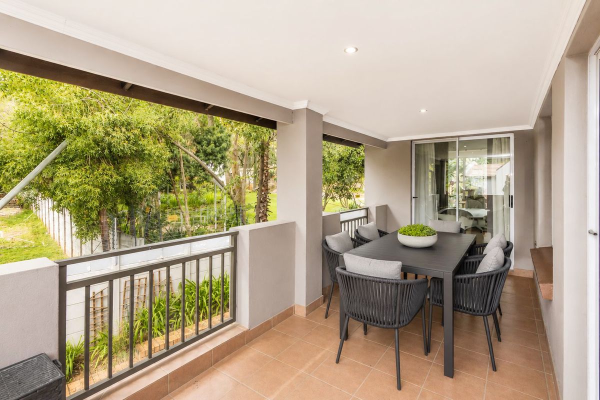 A covered balcony featuring tiled flooring, recessed lighting, and a metal balustrade, providing a pleasant outdoor space with garden views.