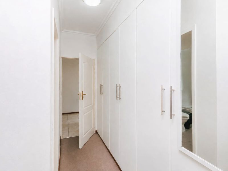 A clean, well-lit hallway featuring extensive built-in storage cupboards with modern handles and a full-length mirrored door.