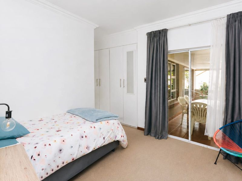 A bright bedroom featuring built-in cupboards, carpeted flooring, and a sliding glass door providing direct access to an outdoor patio area.