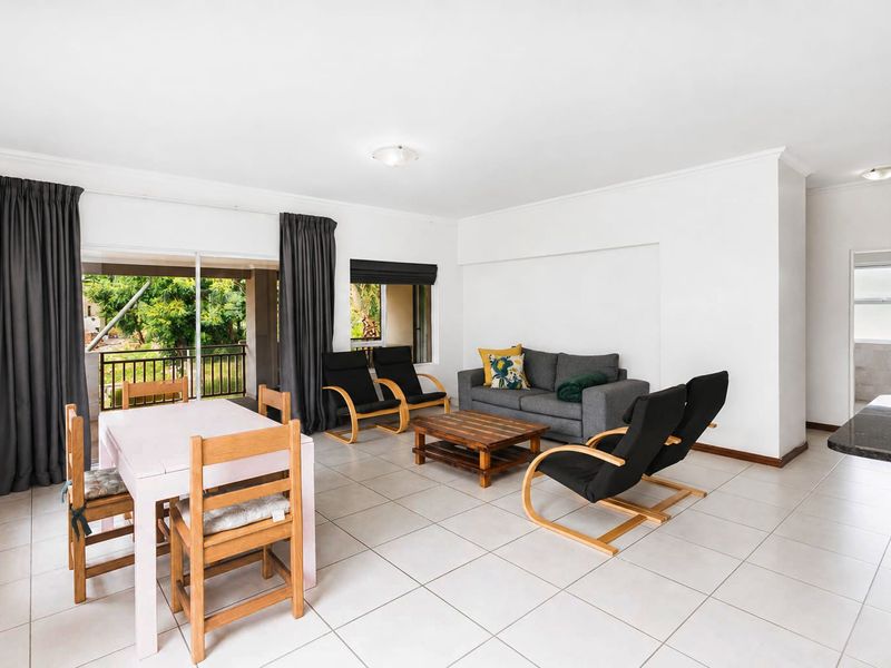 Spacious open-plan living and dining area featuring neutral tiled flooring, large sliding doors leading to a balcony, and a functional kitchen breakfast bar.