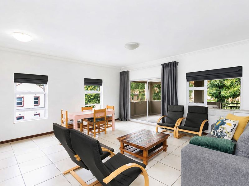 Spacious open-plan living and dining area featuring neutral tiled flooring, large windows, and direct access to a private balcony through sliding glass doors.