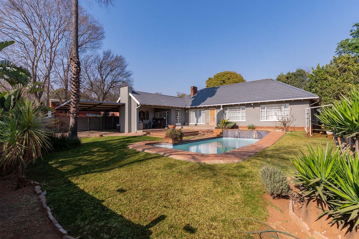 Rear view of the property featuring a swimming pool, covered patio area, carport, and a well-maintained garden with mature trees.