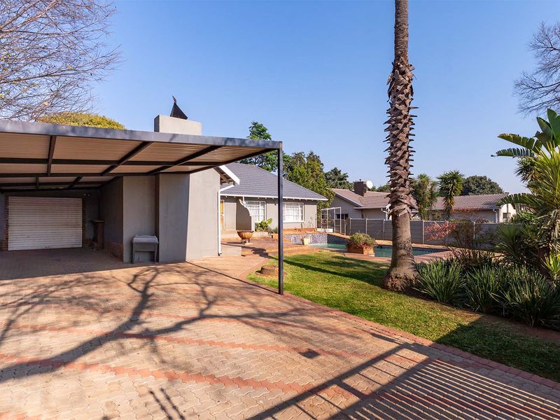 Rear exterior view featuring a paved driveway, covered patio with built-in fireplace, swimming pool, and a well-maintained garden area.