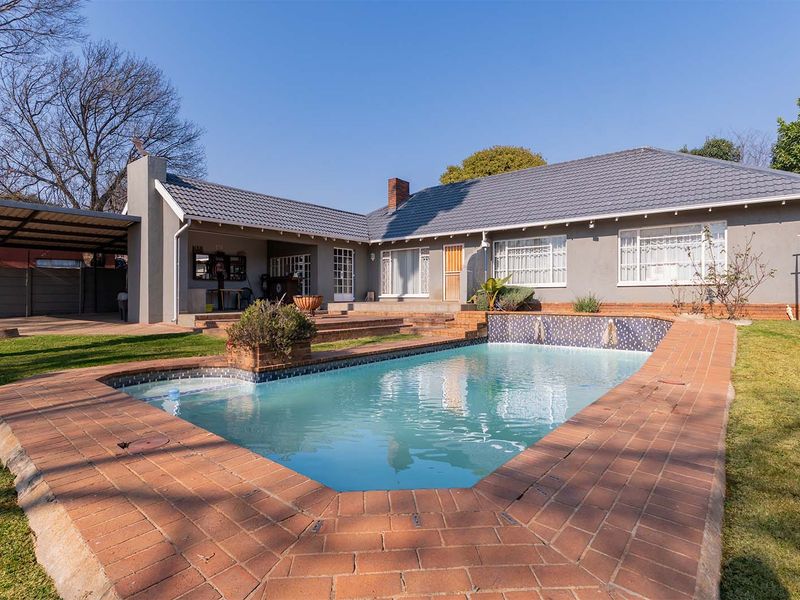 Rear exterior view featuring a swimming pool with brick surround, a covered patio area, and a well-maintained garden.