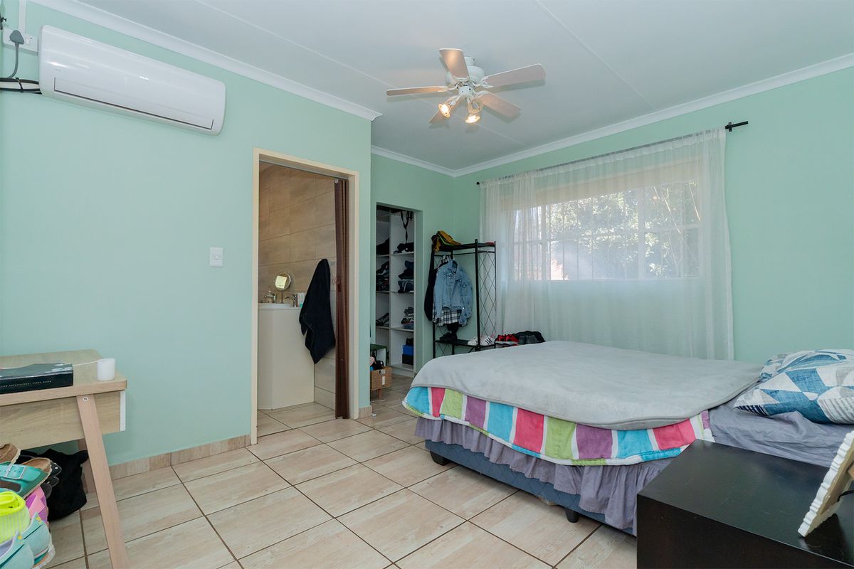 A bedroom featuring tiled flooring, a ceiling fan, an air conditioning unit, and an en-suite bathroom with built-in closet space.