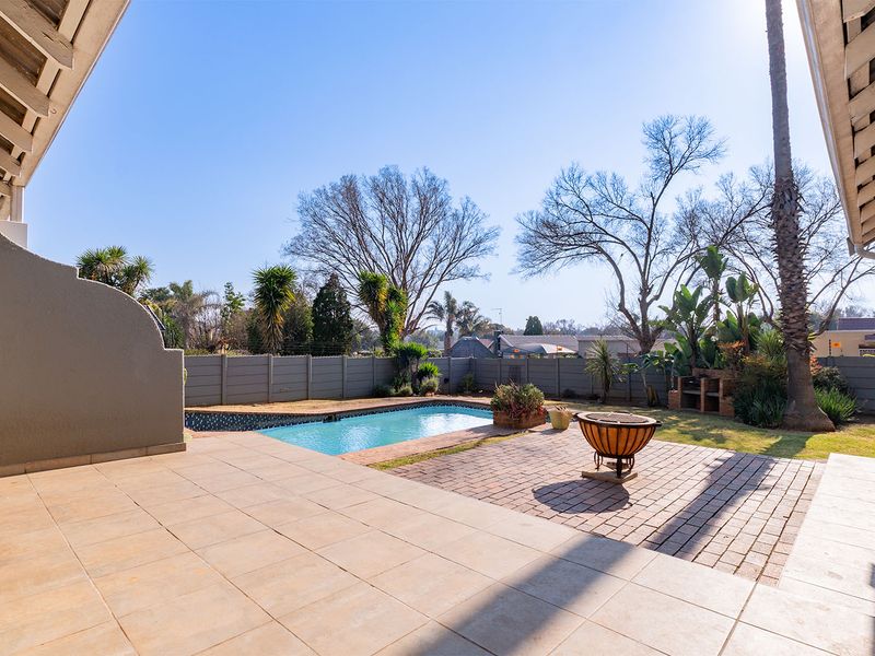 Outdoor entertainment area featuring a swimming pool, brick-paved patio, and a built-in braai, set within a private garden with perimeter walling.