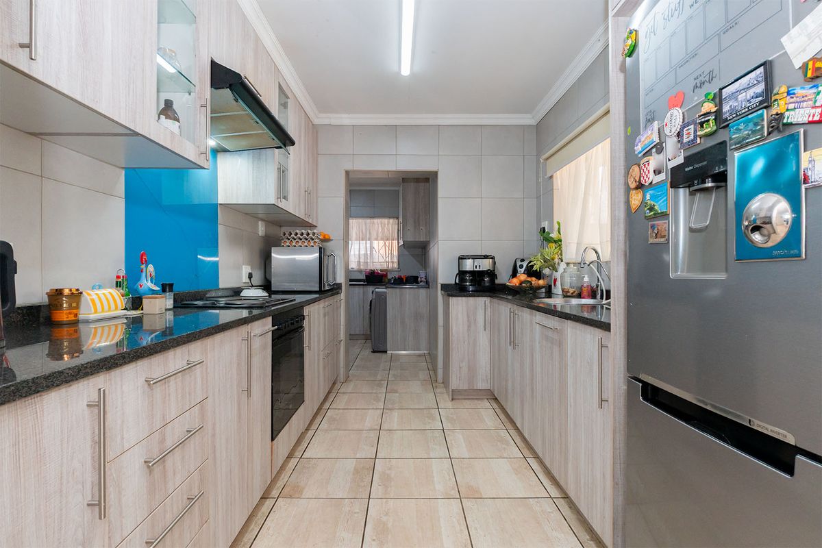 A functional galley-style kitchen featuring light wood-grain cabinetry, granite countertops, a tiled backsplash, and a separate scullery area.