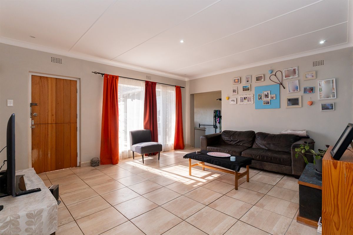 A spacious living room featuring neutral tiled flooring, coved ceilings, and natural light through large windows with direct access to the exterior.