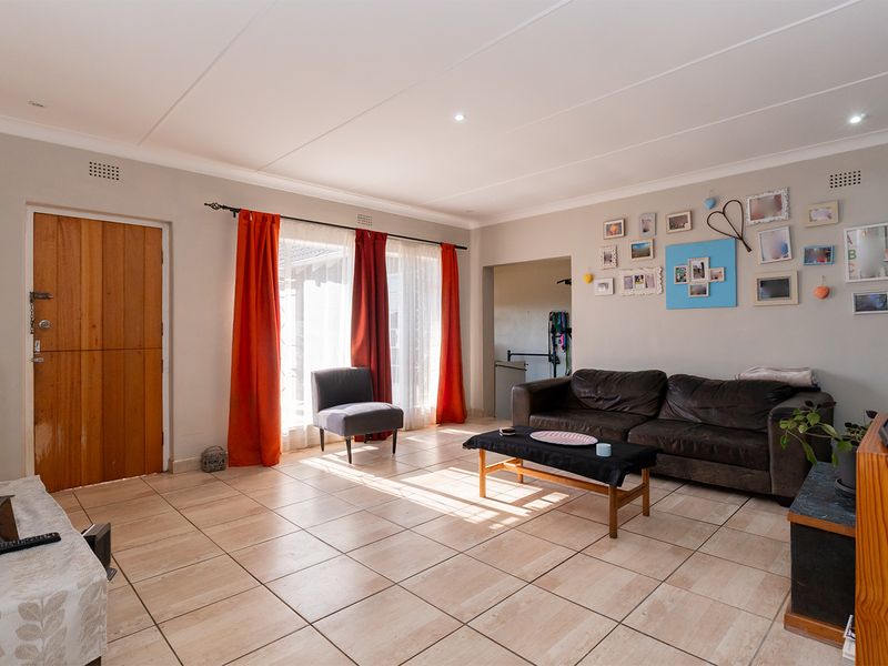 A spacious living room featuring neutral tiled flooring, coved ceilings, and natural light through large windows with direct access to the exterior.