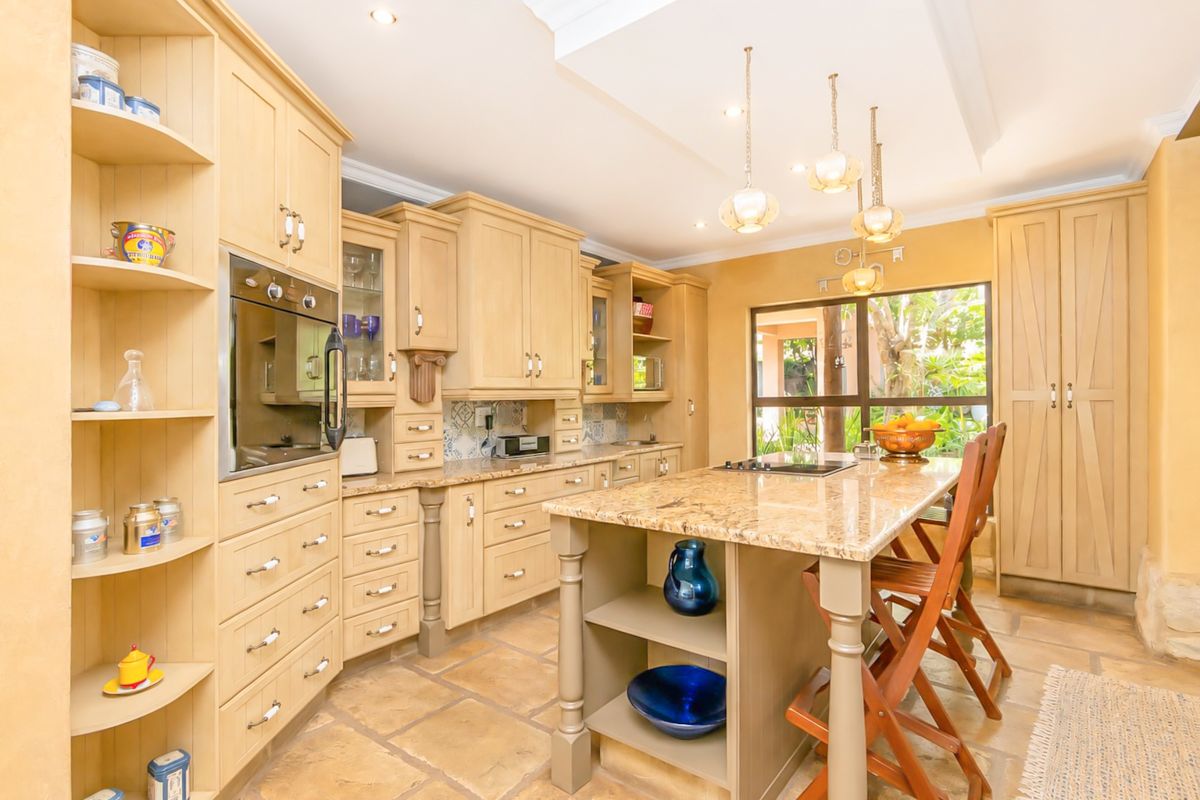 A well-appointed kitchen featuring light wood cabinetry, granite countertops, a central island with seating, and stone tile flooring with natural light.