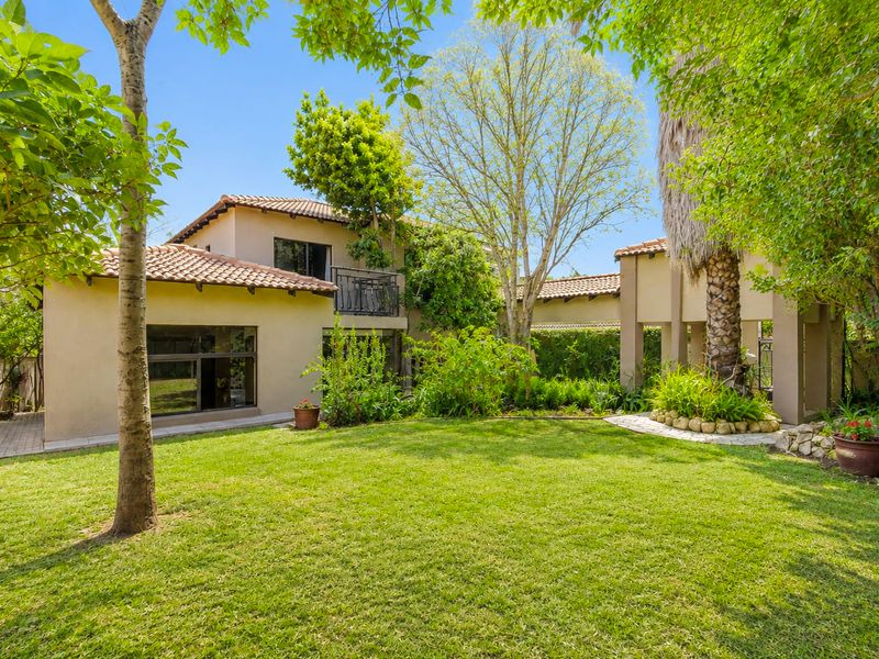 A well-maintained rear garden view featuring a two-story home with terracotta roof tiles, stucco exterior, and a private balcony overlooking the lawn.