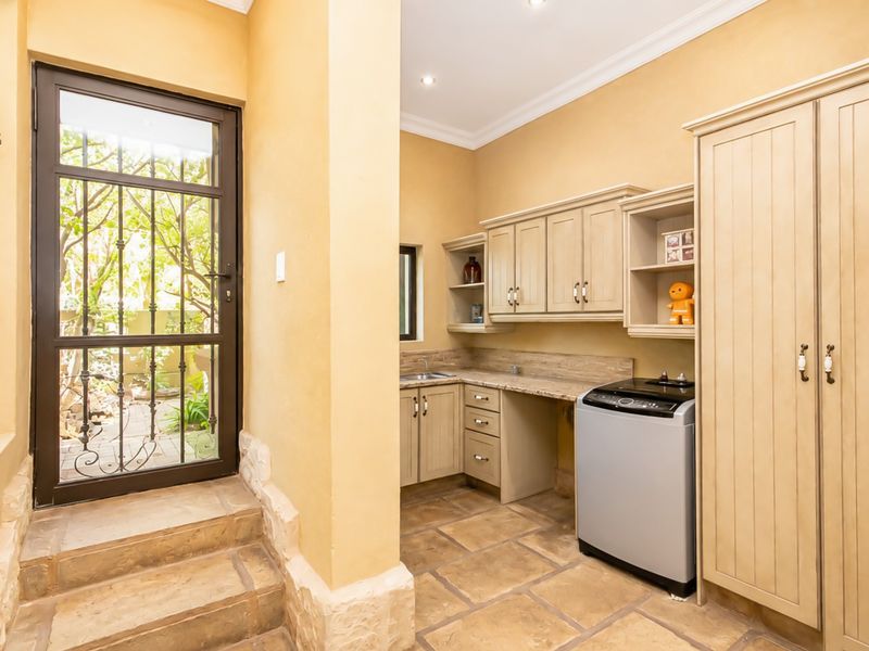 A functional laundry area featuring built-in cabinetry, stone countertops, a sink, and direct access to the garden through a secure door.