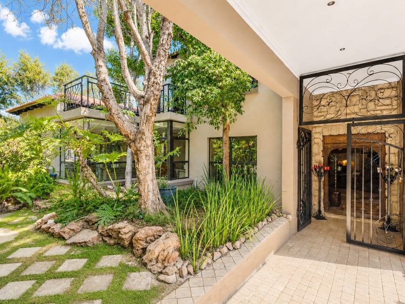 A welcoming front entrance featuring a decorative wrought iron security gate, stone-clad accents, and a landscaped garden area with a paved walkway.