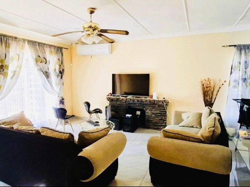 Spacious living room featuring tiled flooring, a stone-clad fireplace, ceiling fan, and split-system air conditioning with access to the outdoors via sliding glass doors.