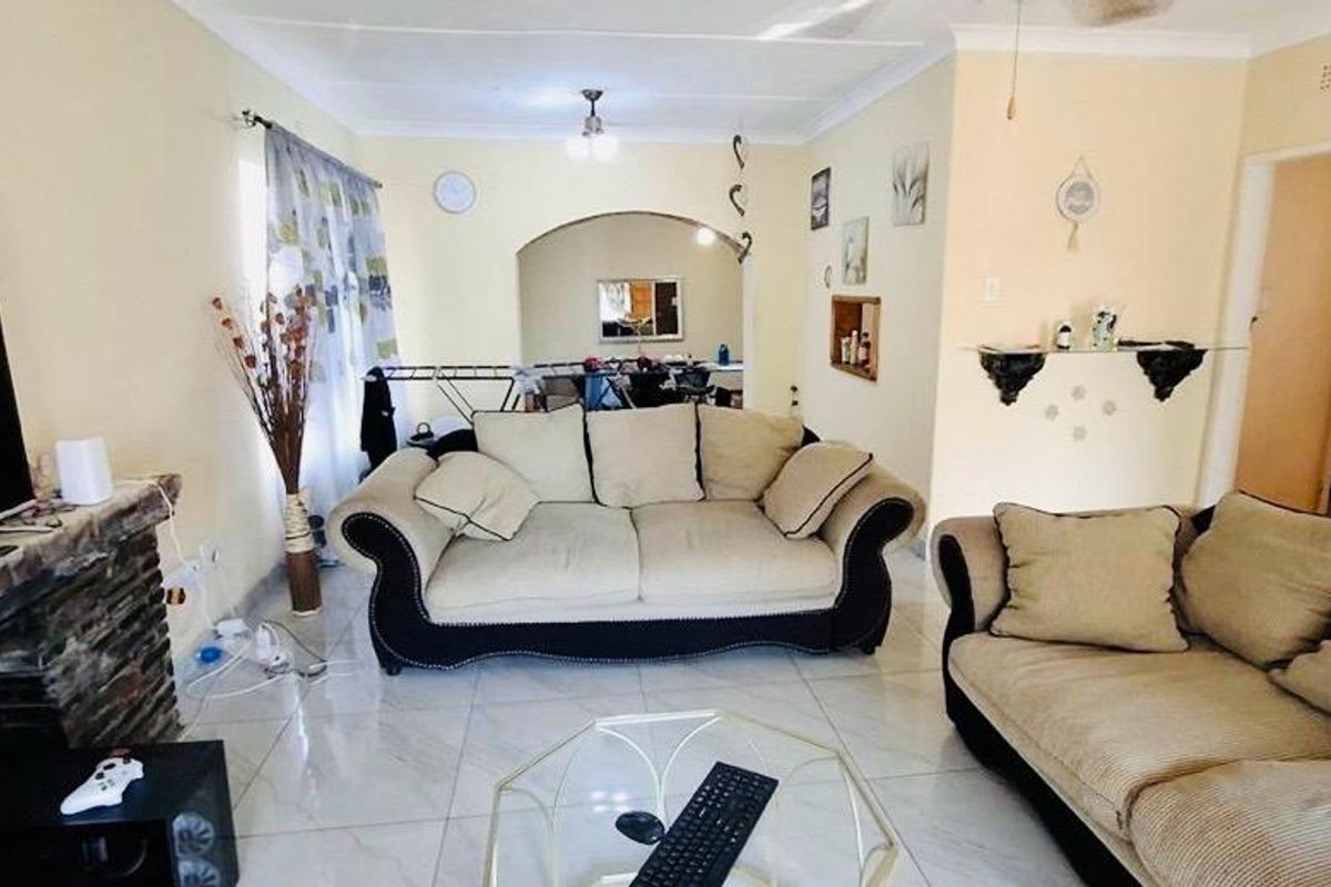 A living room featuring tiled flooring, a stone fireplace, and an arched entryway leading to an adjacent space.