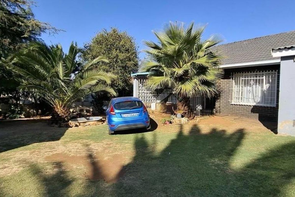 Rear view of the property featuring a lawn, established palm trees, a garage, and a house exterior with security bars on the windows.