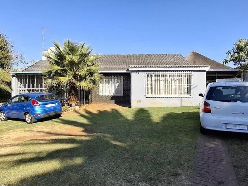 Front view of a single-story residential house featuring a tiled roof, security bars on windows, and a paved driveway with a lawn area.