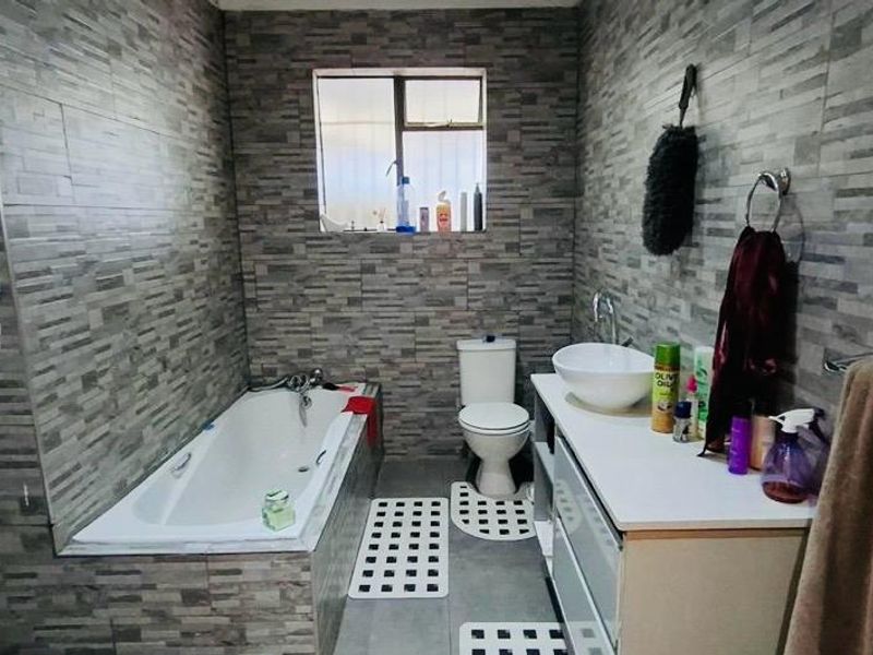 A modern bathroom featuring grey stone-look wall tiles, a built-in bathtub, a vanity with a vessel sink, and a toilet.