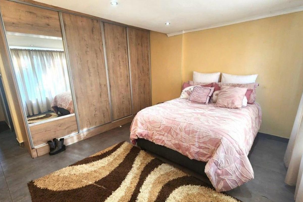 A well-maintained bedroom featuring modern wood-finish built-in wardrobes with mirrored panels, recessed ceiling lighting, and neutral tiled flooring.
