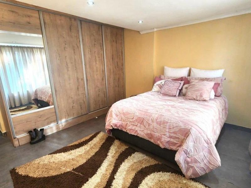 A well-maintained bedroom featuring modern wood-finish built-in wardrobes with mirrored panels, recessed ceiling lighting, and neutral tiled flooring.