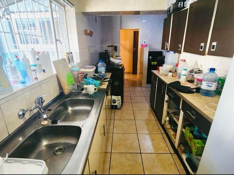 A functional kitchen featuring a double bowl stainless steel sink, tiled splashbacks, and built-in cabinetry with some missing doors.