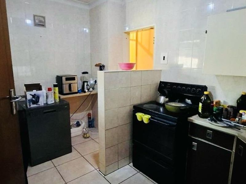 A functional kitchen featuring tiled walls and flooring, built-in cabinetry, and a freestanding stove, offering a practical layout with potential for modern updates.