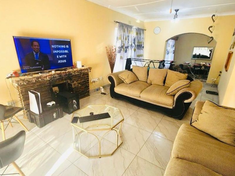 A living room featuring tiled flooring, a stone-clad fireplace, and an arched entryway leading to an adjacent space.