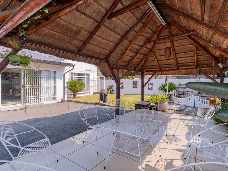 Covered outdoor patio area featuring a traditional thatched roof, timber support structure, and tiled flooring, overlooking a private garden and lawn.