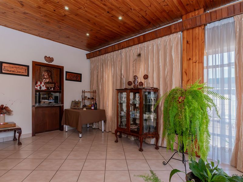 A living area featuring a warm timber-clad ceiling, recessed lighting, ceramic tiled flooring, and a built-in bar nook with decorative shelving.