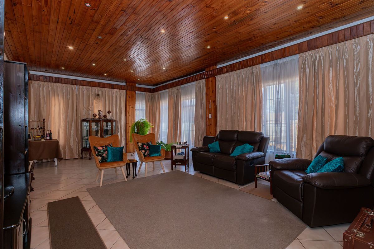 Spacious living room featuring a warm timber tongue and groove ceiling, recessed lighting, and large windows with floor-to-ceiling curtains.