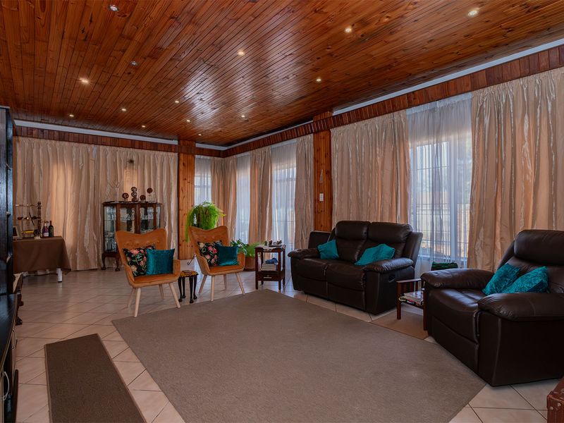 Spacious living room featuring a warm timber tongue and groove ceiling, recessed lighting, and large windows with floor-to-ceiling curtains.