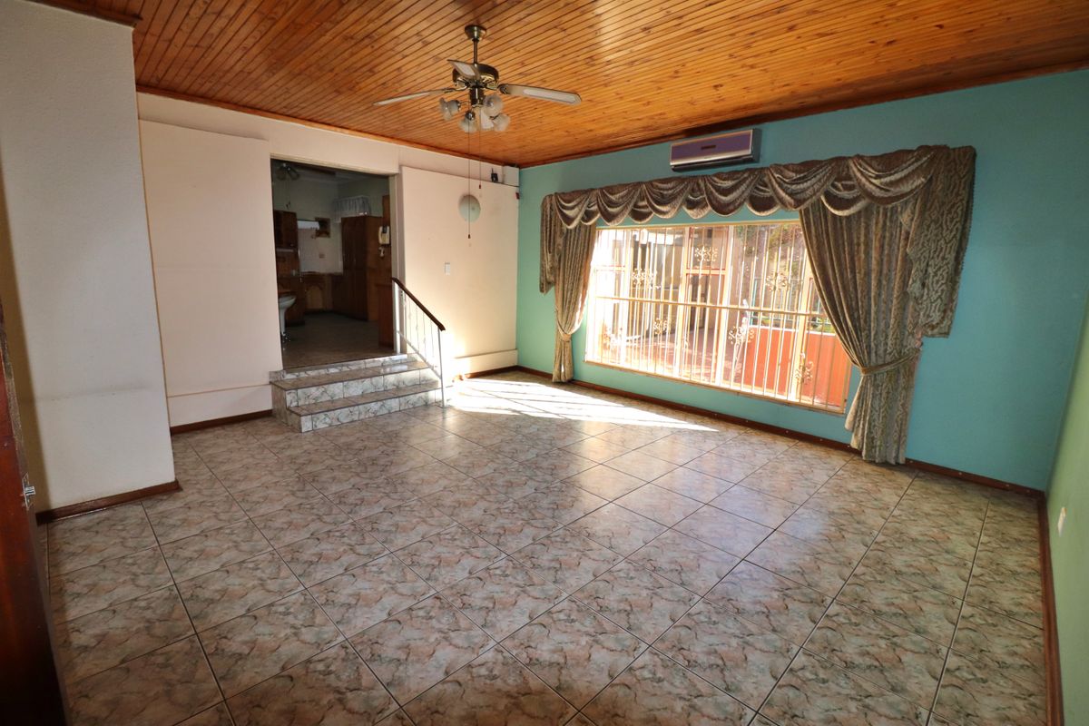 Spacious living area featuring timber tongue and groove ceilings, tiled flooring, and a split system air conditioner, with steps leading to an adjacent room.