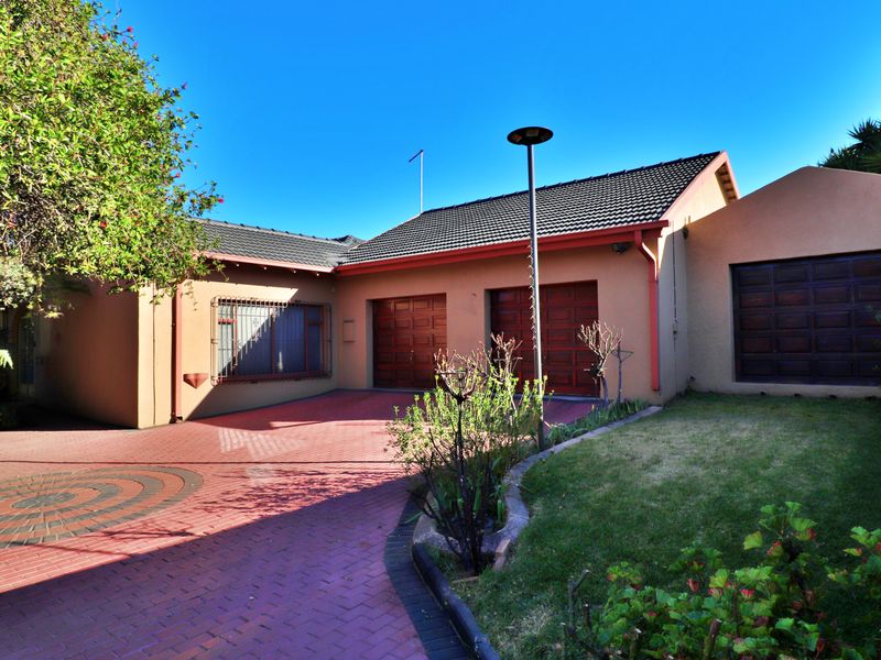 Front exterior view of the property featuring a triple garage, paved driveway, and landscaped garden area.