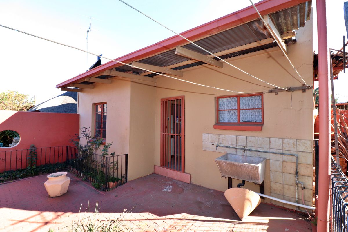 Rear exterior view of the property featuring a paved patio area, a built-in utility sink, and a covered walkway with security gate access.