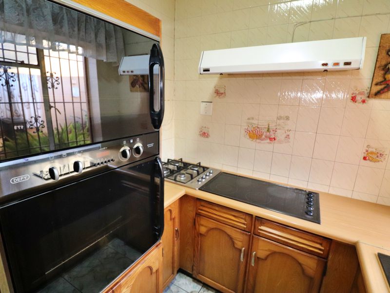 A functional kitchen featuring wooden cabinetry, a dual gas and electric hob, built-in oven, and tiled splashback with decorative accents.