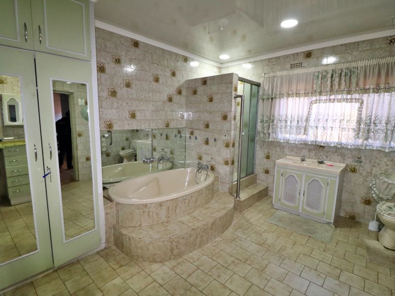 Spacious bathroom featuring a sunken bathtub, separate shower enclosure, built-in vanity, and extensive wall tiling with a traditional aesthetic.