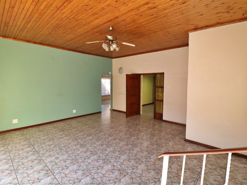 An empty living room featuring a timber ceiling, ceiling fan, and tiled flooring, providing a blank canvas for potential interior updates.